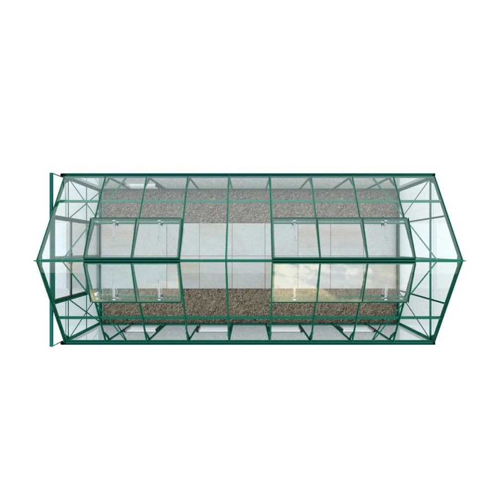 A rectangular glass Rhino Greenhouse with a green metal frame sits on pebbled ground, featuring multiple roof vents for ventilation. The surrounding area appears to be open and unobstructed.