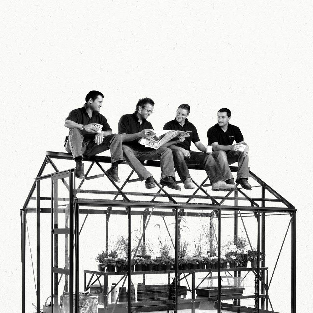 Four men sit on a Rhino Greenhouse roof, chatting and reading papers. Below, plants are arranged on shelves, indicating a gardening or Rhino Greenhouse setting.
