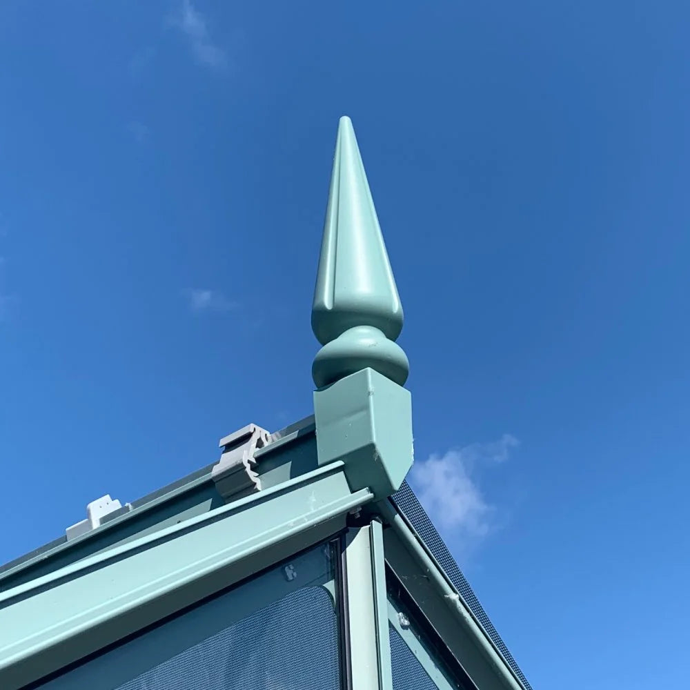 A decorative finial tops a Rhino Greenhouse structure against a bright blue sky, highlighting its sleek, modern design and sturdy construction.