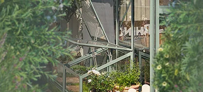 Rhino Greenhouse with sturdy metal frame and lush plants inside; surrounded by greenery. Partial text visible: RHI... London.